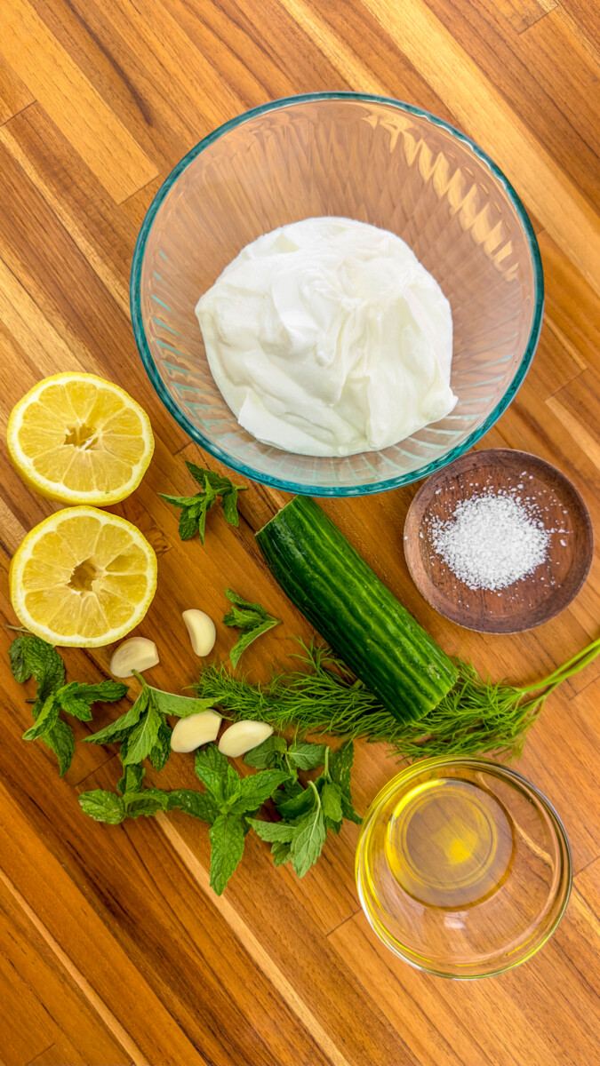 An array of fresh ingredients needed for a tzatziki sauce recipe arranged on a kitchen counter.