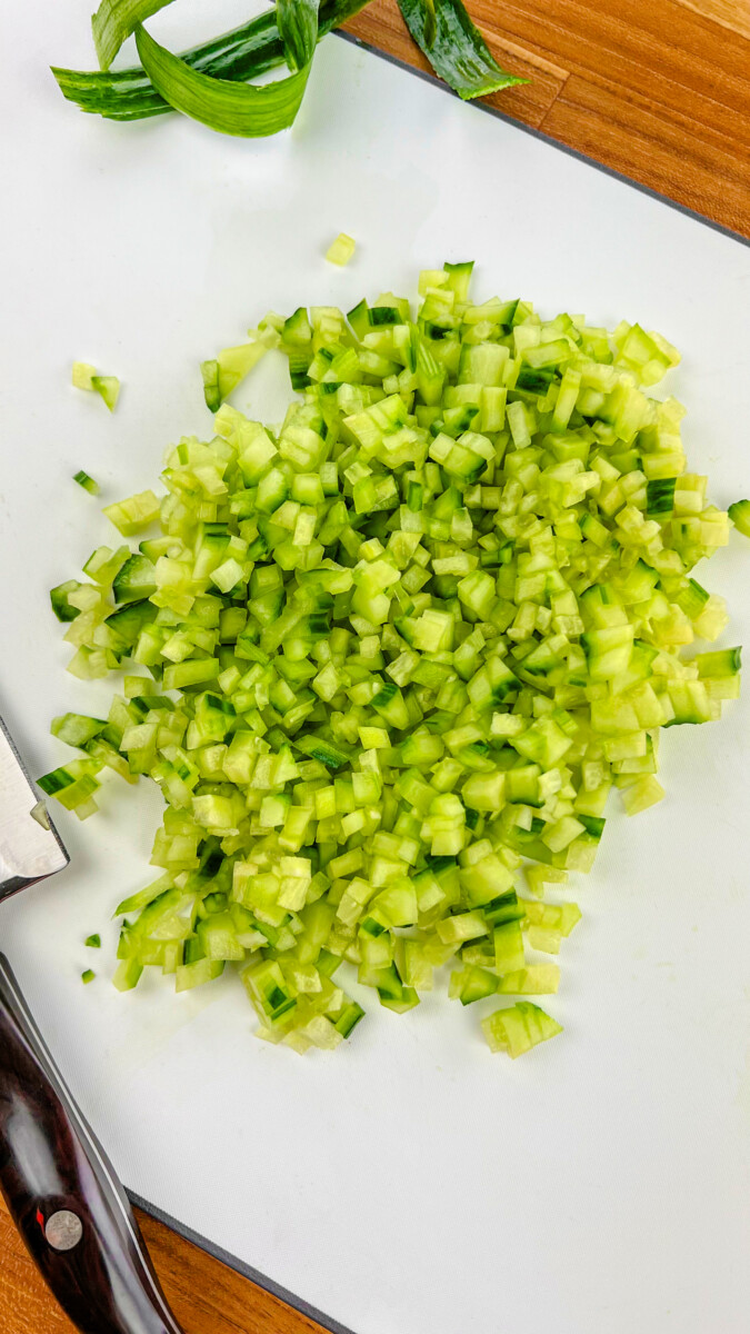 Diced cucumber sprinkled with salt, resting on a paper towel inside a colander for excess water removal.