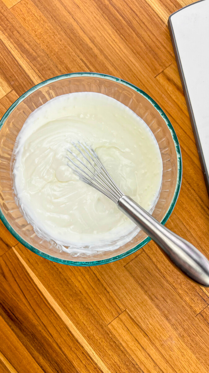 Whisking Greek yogurt in a mixing bowl.