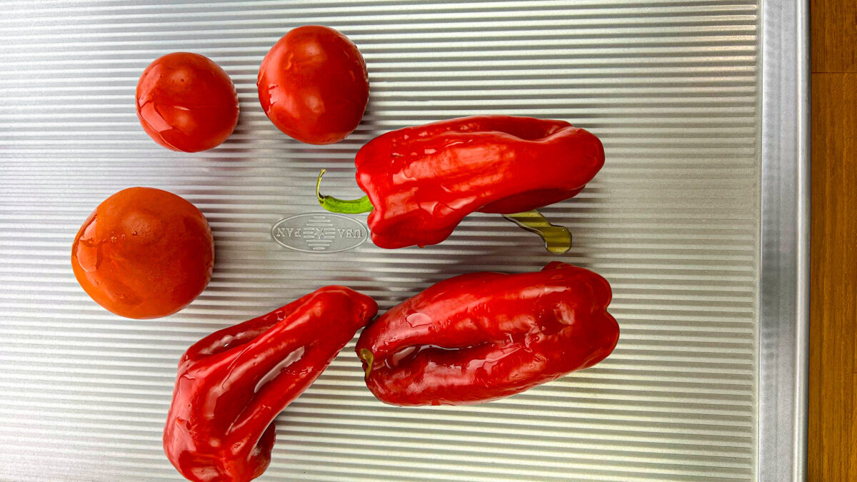 Bell peppers and tomatoes arranged on a baking sheet, ready for roasting.