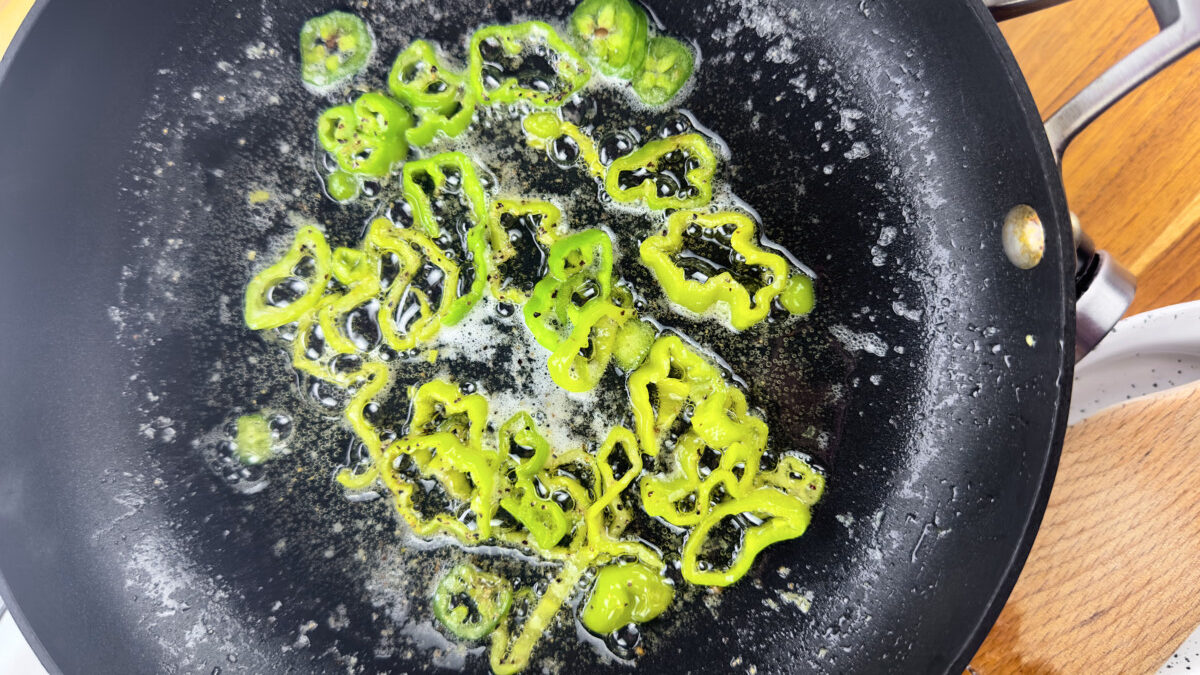 Green bell pepper and jalapeño sautéing in olive oil, seasoning with salt and pepper