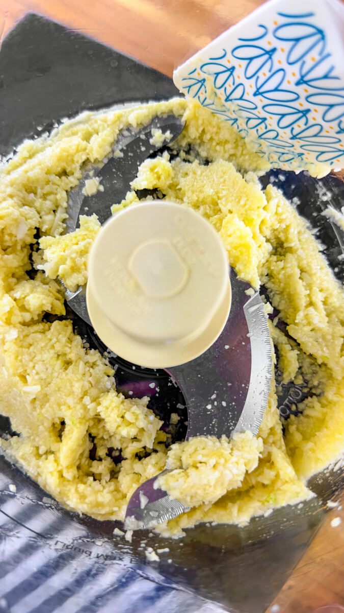 Adding oil to the garlic-salt paste in a food processor.