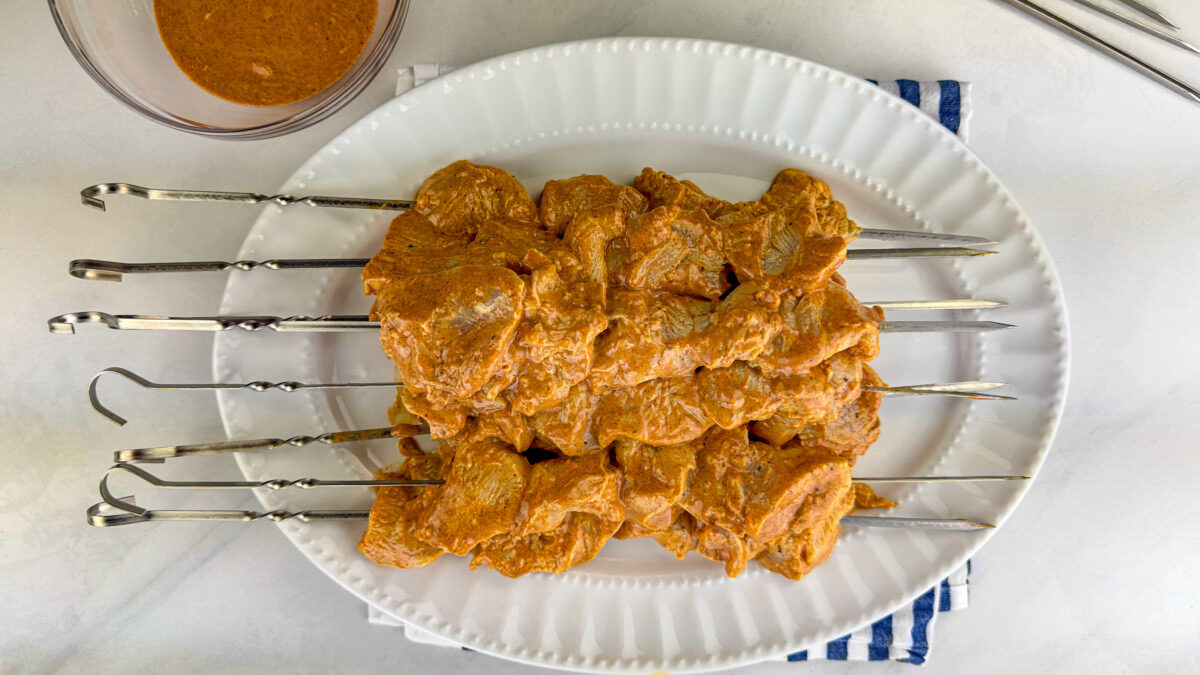 Marinated chicken pieces being threaded onto skewers.