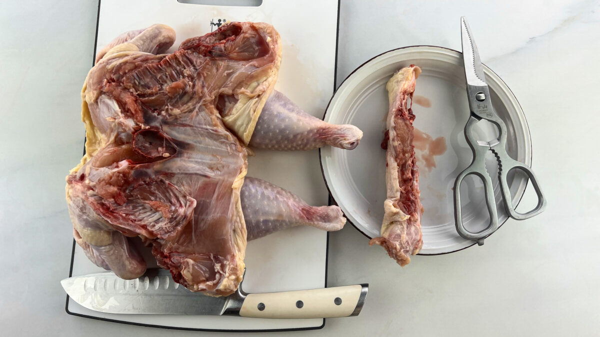 A clean chicken with the backbone removed, lying flat on a table next to a pair of kitchen shears.