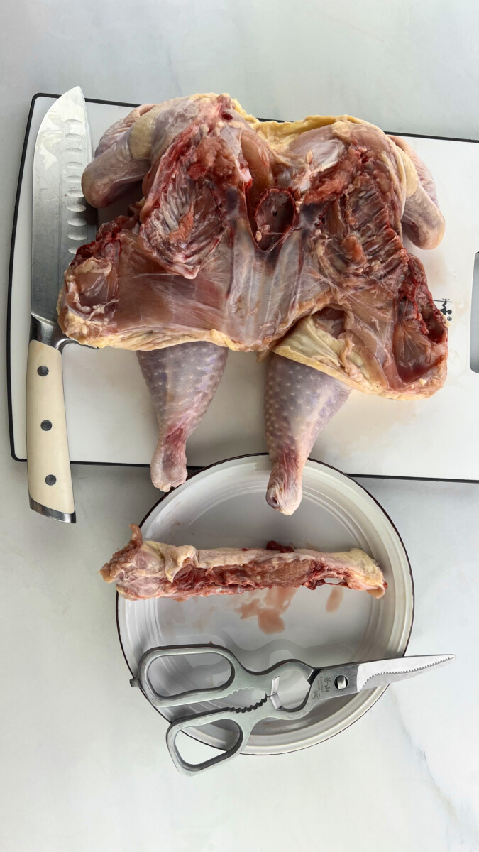 A clean chicken with the backbone removed, lying flat on a table next to a pair of kitchen shears.