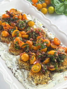 Plated dish showcasing crispy Japanese eggplant recipe layers of creamy yogurt sauce, golden-brown eggplant pieces, crowned with vibrant tomato salsa.