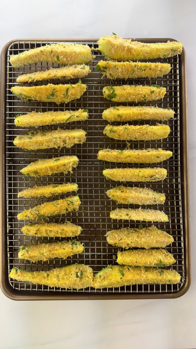 Tray of prepped zucchini fries lined on a baking rack, ready for oven-baking at 400°F.