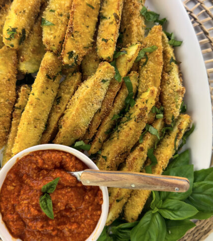 Golden-browned zucchini fries served alongside a vibrant bowl of fresh romesco sauce.