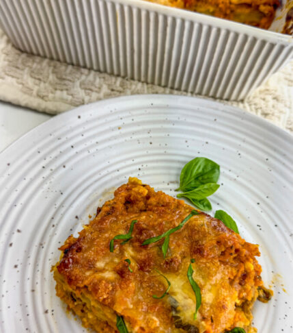 Eggplant Parmigiana served on a plate next to the main dish, topped with fresh basil leaves.