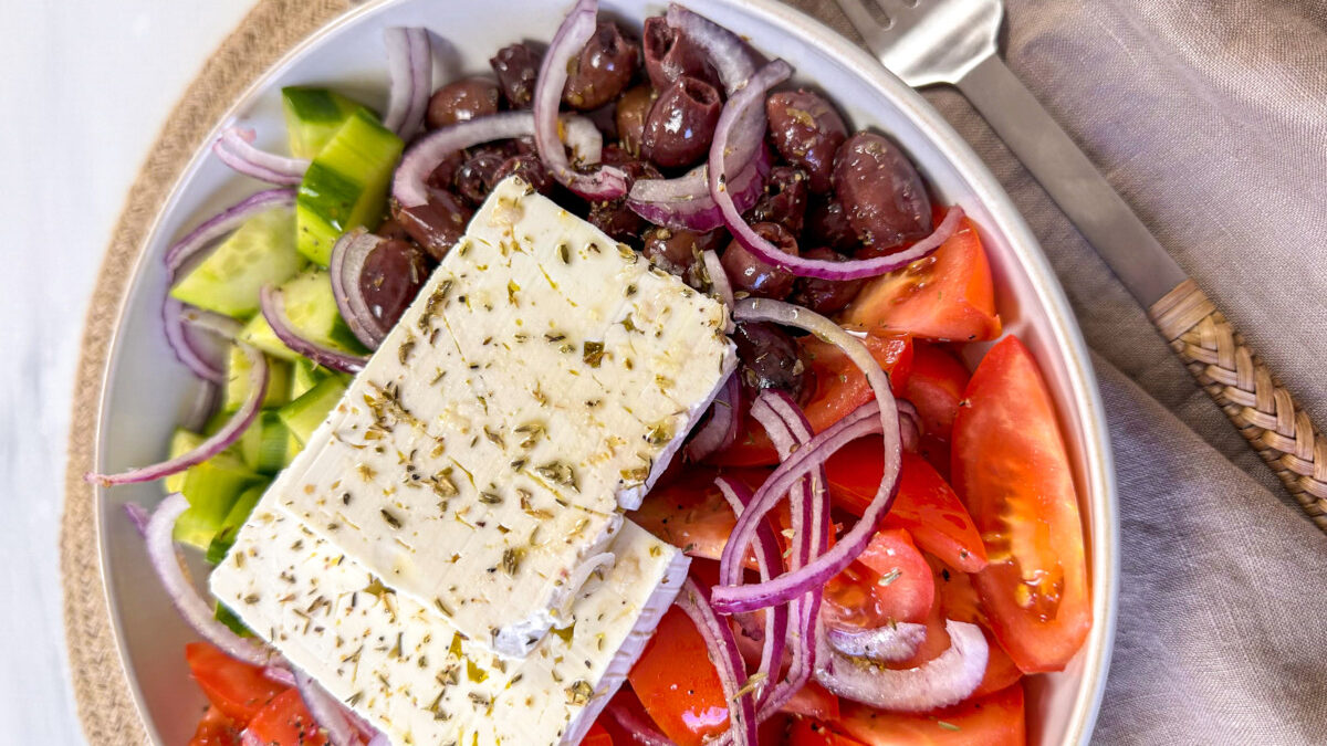 A plate of Traditional Greek Salad, known as Horiatiki in Greece, epitomizes Greek simplicity and flavor. This rustic Salad is a colorful combination of ripe tomatoes, crisp cucumbers, sharp red onions, and green bell peppers.