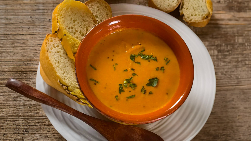 Bowl of vibrant Carrot Coconut Soup garnished with fresh herbs.
