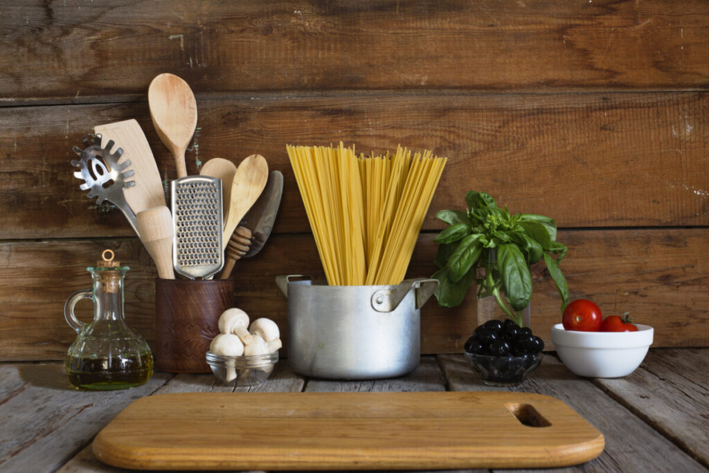 Spaghetti standing in a pot on the counter, surrounded by essential Mediterranean ingredients like olive oil, basil, and tomatoes.
