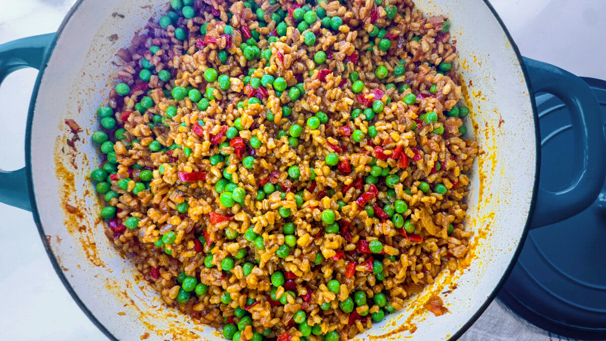 Green peas being stirred into a skillet of hot farro, completing the dish.