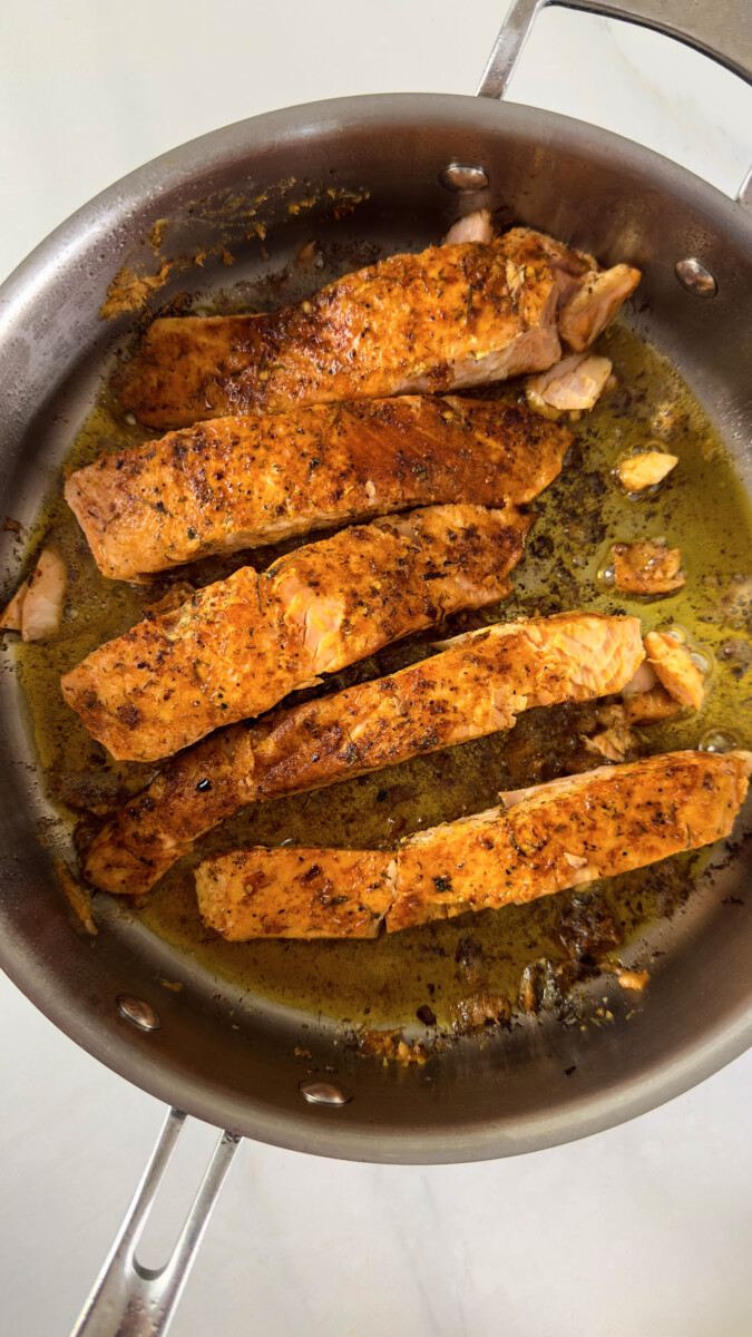 Salmon filets being cooked skin-side down in a hot skillet with olive oil.