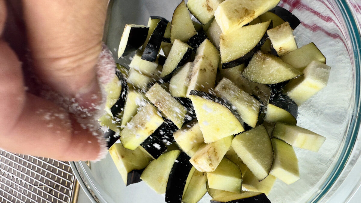 Sprinkling a generous amount of salt over cubed eggplant for Pasta alla Norma recipe preparation.