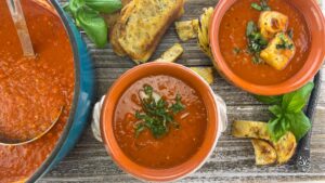 Two bowls of tomato basil soup, the main pot, and a side of tempting croutons.