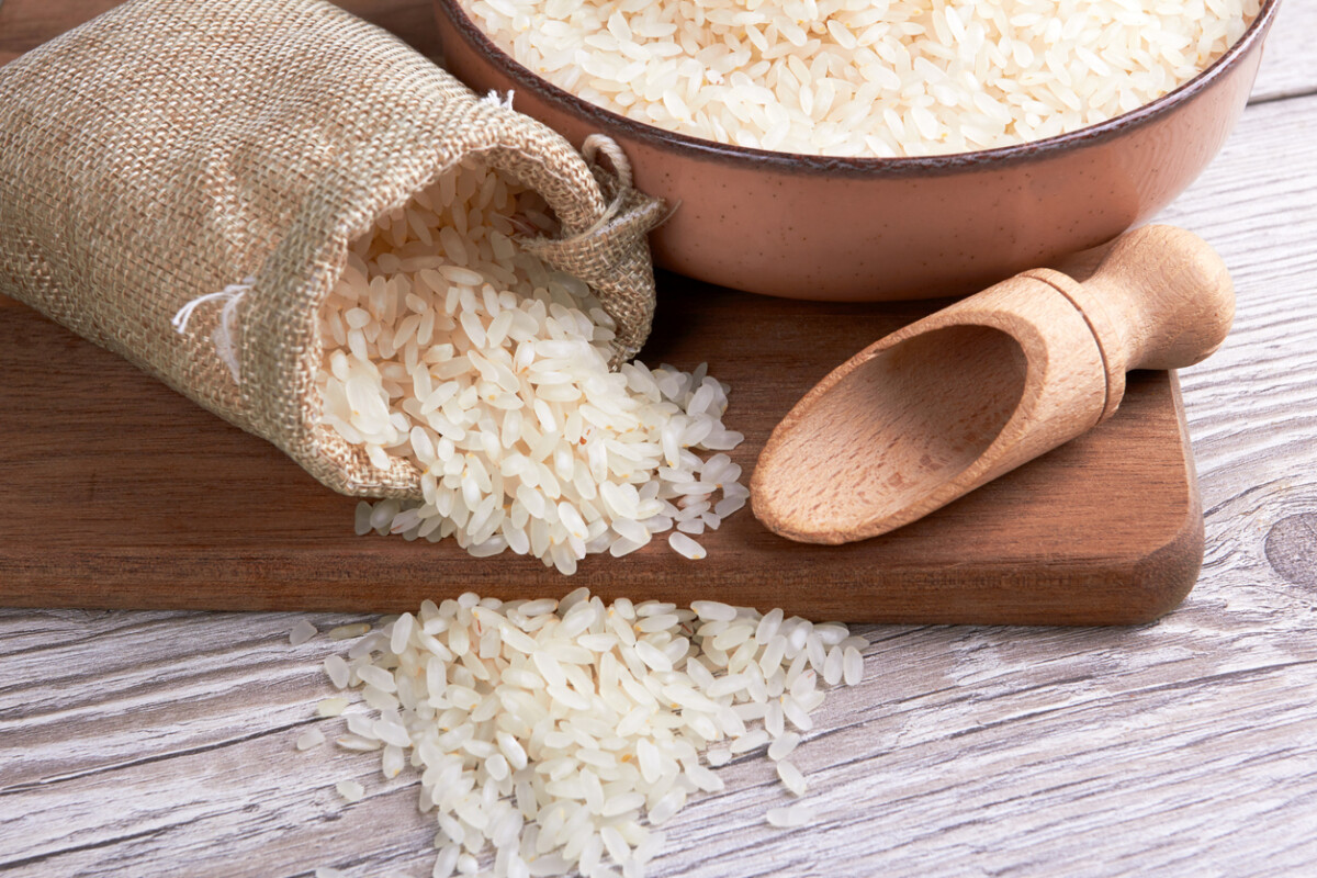 Bag of rice, pot, and wooden spoon on a wooden surface – the essential trio for creating delicious meals.