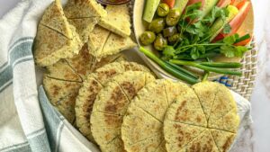 Freshly baked Kesra Bread surrounded by vibrant herbs, olives, and vegetables.