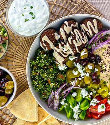Falafel bowl with hummus and tabouleh drizzle with tahini salad served with olives, taziki sauce, tahini salad.