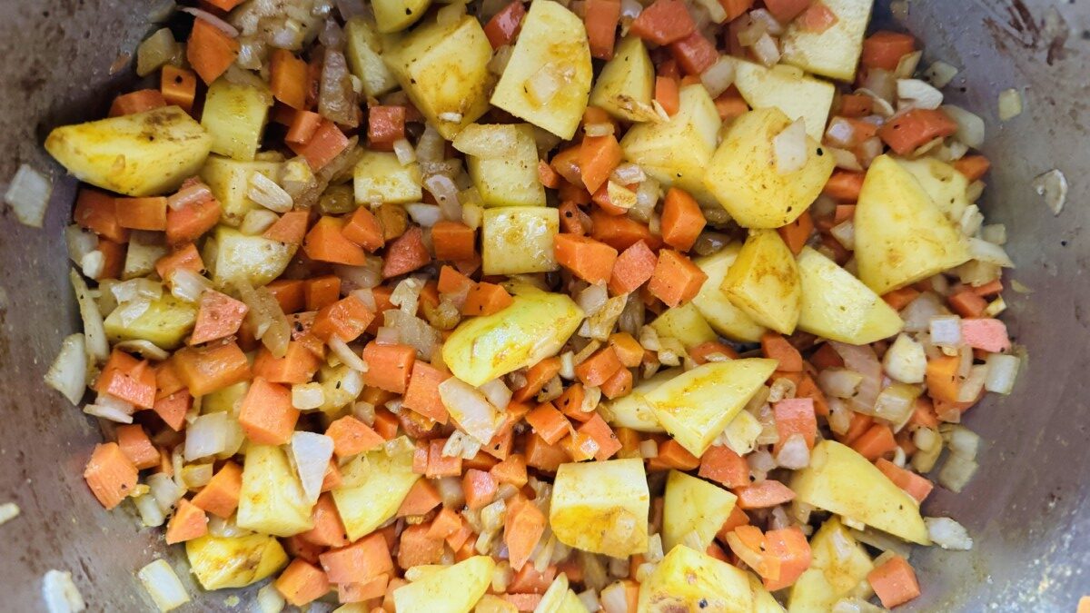 Chopped carrots and potatoes being sautéed in olive oil and garlic in a pot with beef