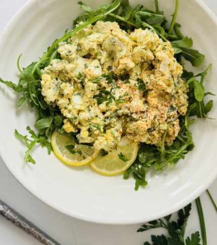 No-mayo egg salad served over a bed of arugula in a bowl with a spoon beside it.