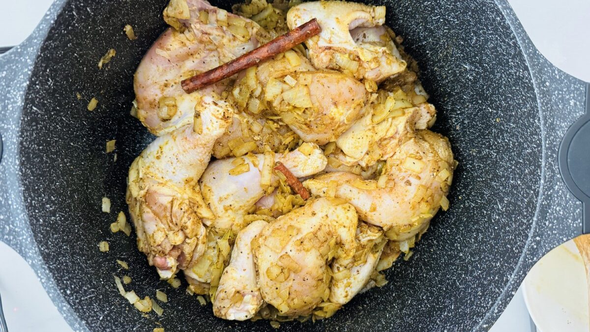 Sliced chicken pieces in a pot with golden brown, sautéed onions and a sprinkle of spices. A spoon is stirring the mixture to ensure even browning.