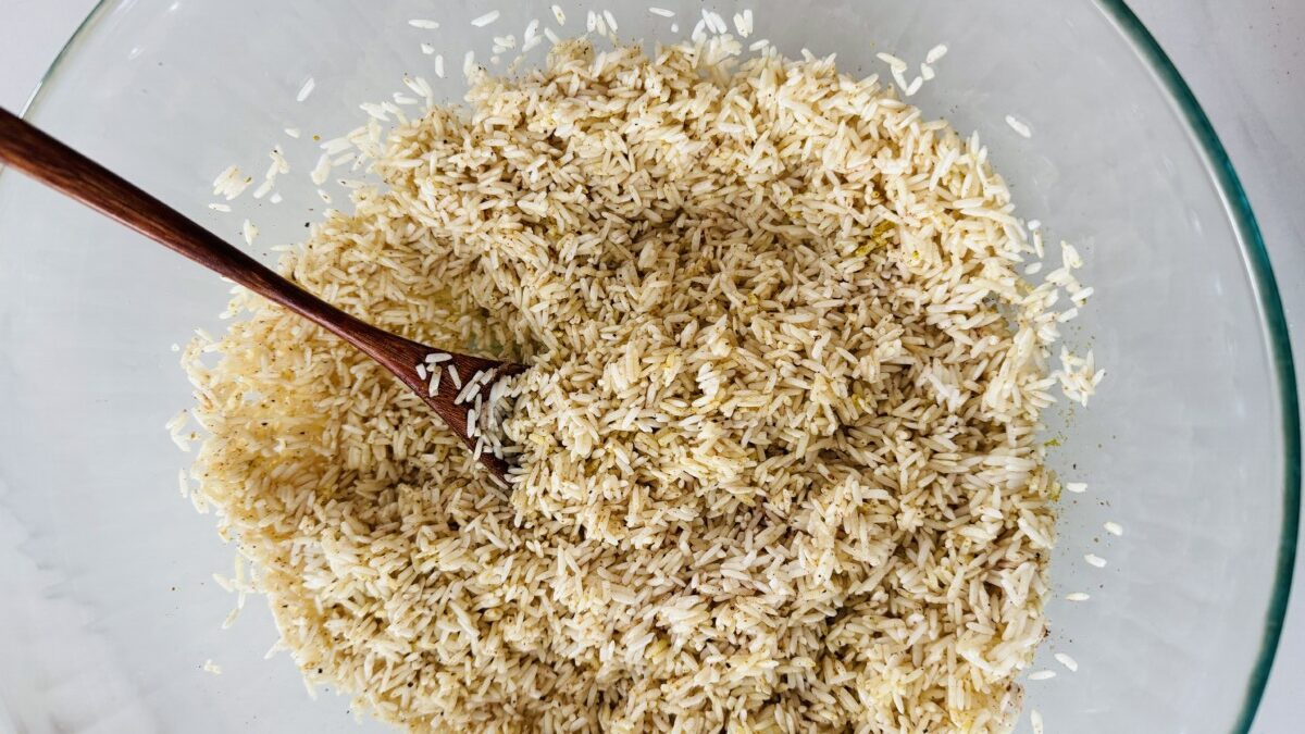 A bowl filled with white basmati rice with colorful whole spices like cardamom pods, cloves, and bay leaves scattered and mixed throughout the grains.