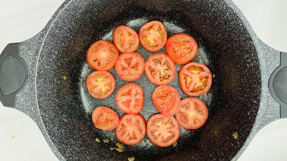 Sliced red tomatoes arranged in a single layer at the bottom of a pot.