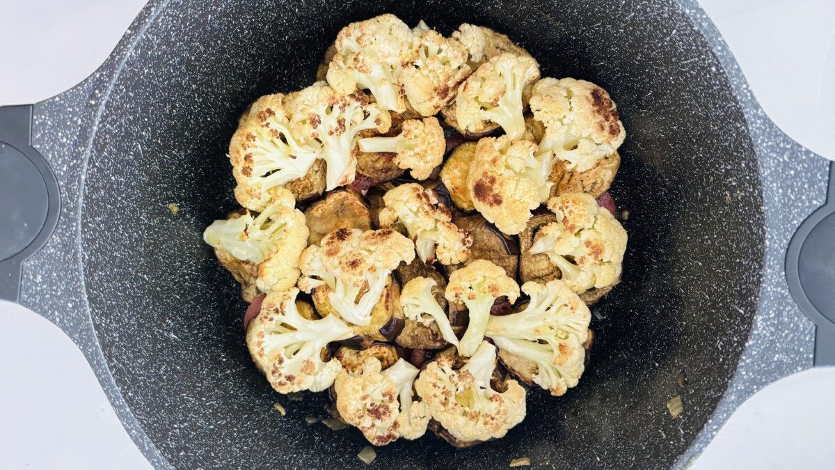 Roasted cauliflower florets arranged in a single layer on top of sliced roasted eggplant in a pot.
