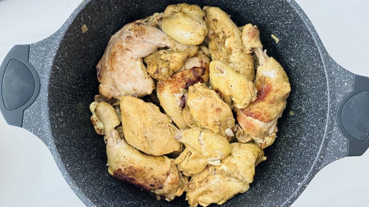 A layer of browned chicken pieces arranged in a single layer on top of roasted cauliflower florets in a pot.
