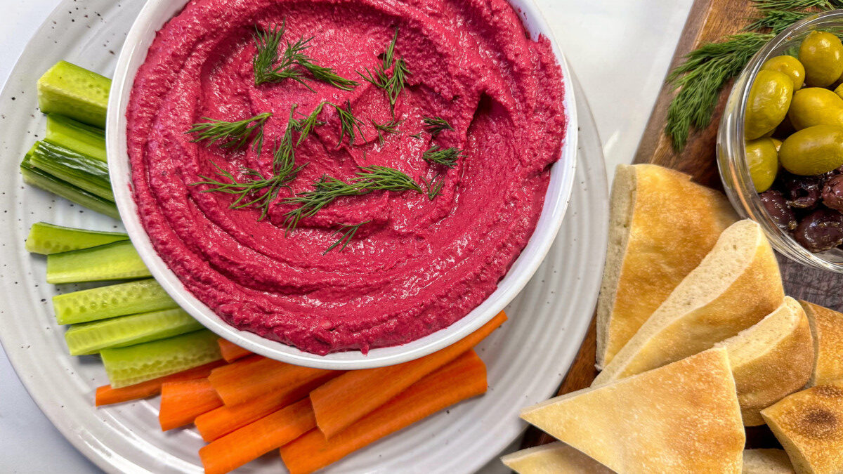 A platter of beet hummus, some fresh veggies, pita bread and some olives 