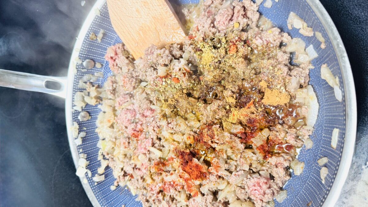 Ground meat cooked with onions and Mediterranean spices in a skillet, ready to be used for stuffing pasta shells.