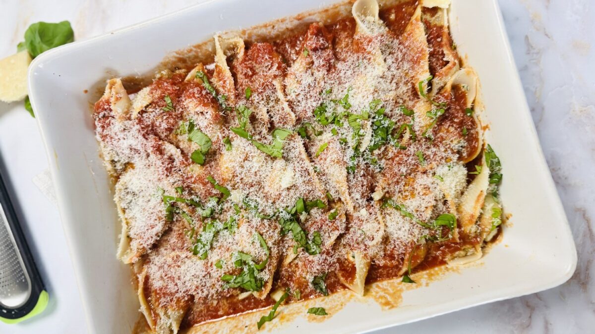 Stuffed pasta shells topped with rich tomato sauce and sprinkled with parmesan cheese, ready to bake.