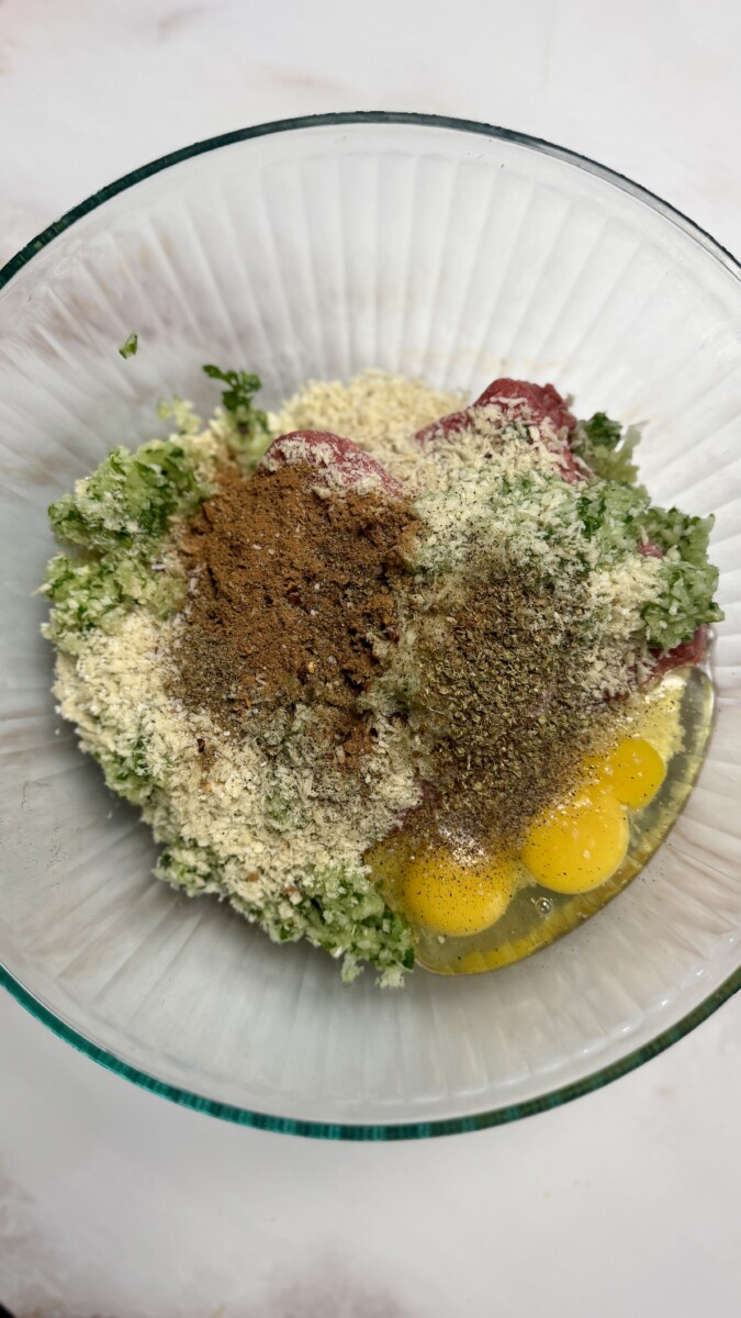 Garlic, onion, and parsley mixture added to a bowl with ground beef, panko breadcrumbs, and eggs, ready to be mixed for Greek meatballs.