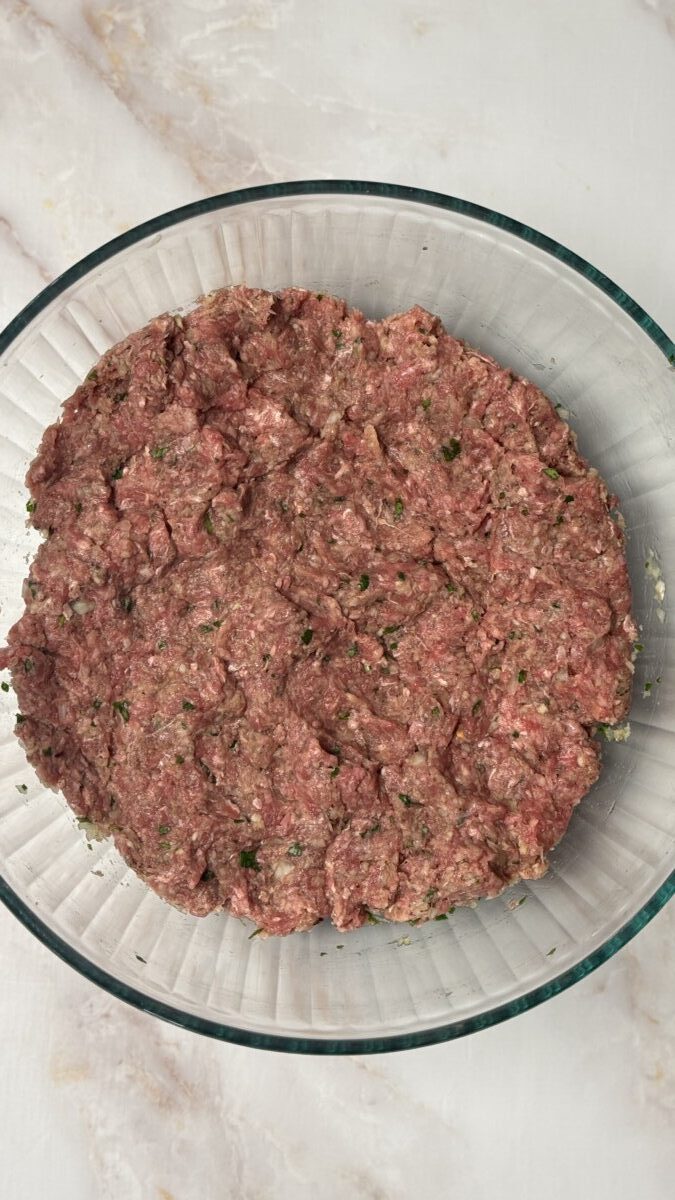 Greek meatball mixture with ground beef, spices, and herbs fully mixed in a bowl, ready to be shaped into meatballs.