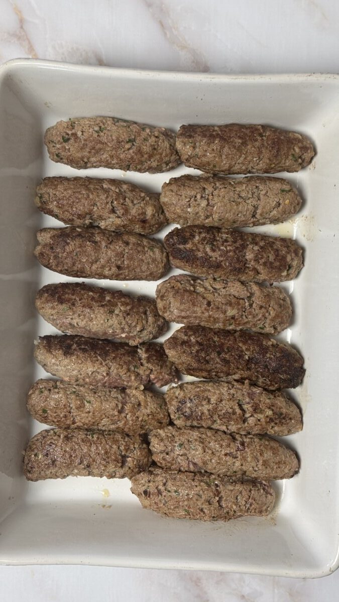 Shaped Greek meatballs arranged neatly in a large deep baking dish, ready for tomato sauce and baking.