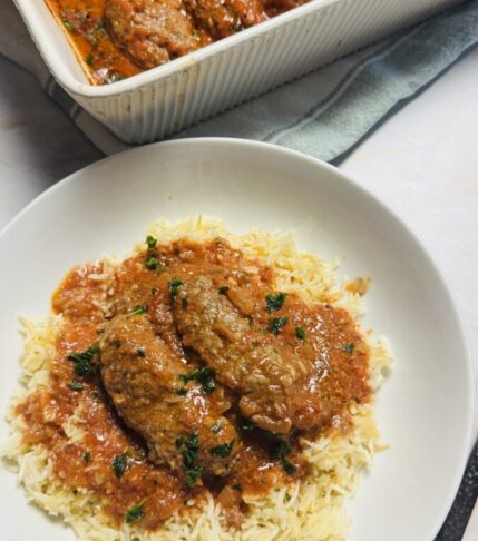 Greek meatballs in tomato sauce served over a bed of fluffy white rice, garnished with fresh parsley.