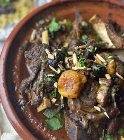 Finished lamb tagine served in a tagine pot alongside fluffy couscous, garnished with fresh herbs and almonds.