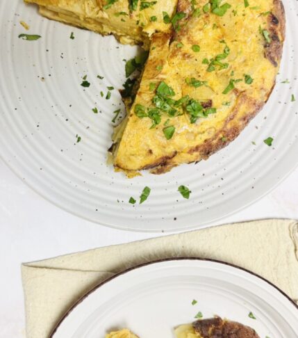 A large piece of Spanish Omelet on a big serving plate, with a smaller slice on a separate plate, garnished with parsley