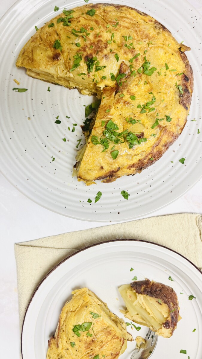 A large piece of Spanish Omelet on a big serving plate, with a smaller slice on a separate plate, garnished with parsley