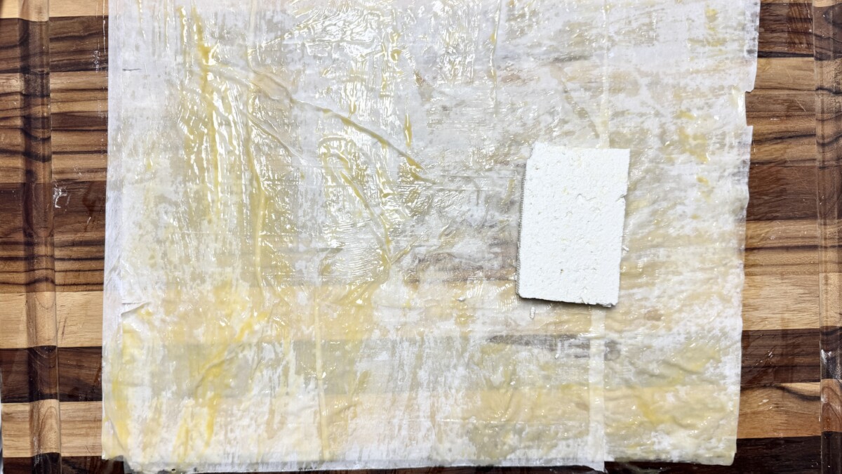 A block of feta placed in the center of double layers of phyllo dough brushed with an egg, butter, and olive oil mixture.