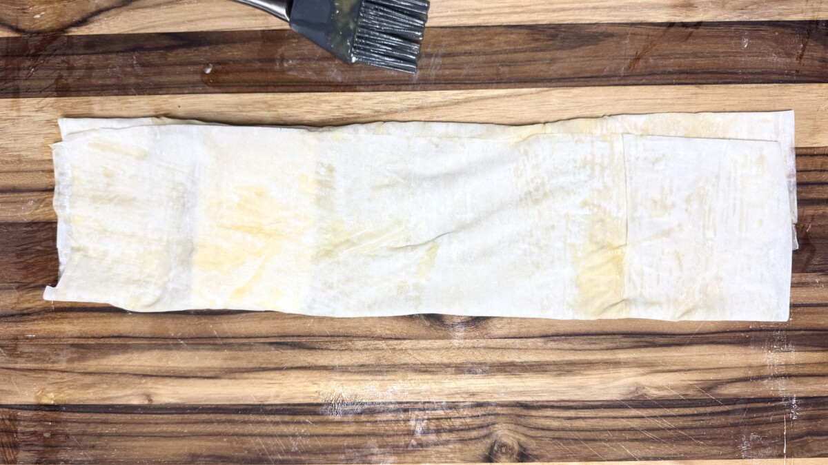 Phyllo dough sides folded over a block of feta, partially wrapping it before baking.