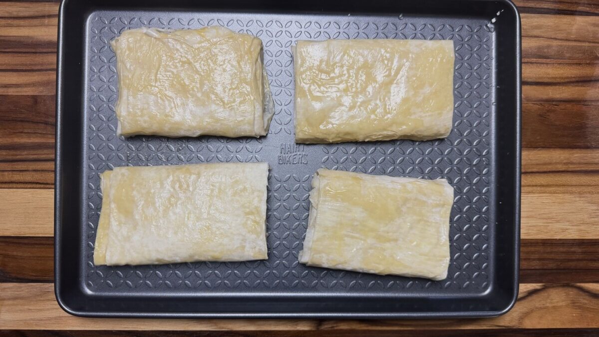 Four pieces of feta wrapped in phyllo dough placed on a baking sheet, ready to go into the oven.