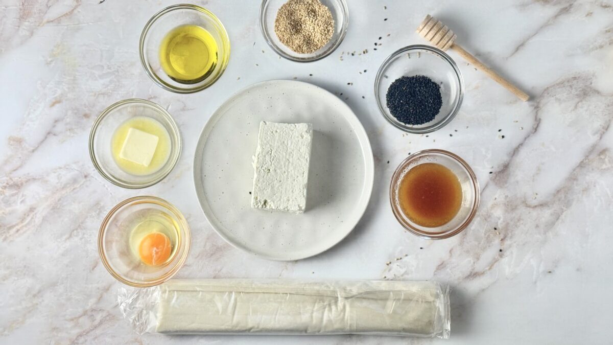 All the ingredients for Greek baked feta in phyllo, including feta cheese, phyllo dough, honey, sesame seeds, and olive oil.