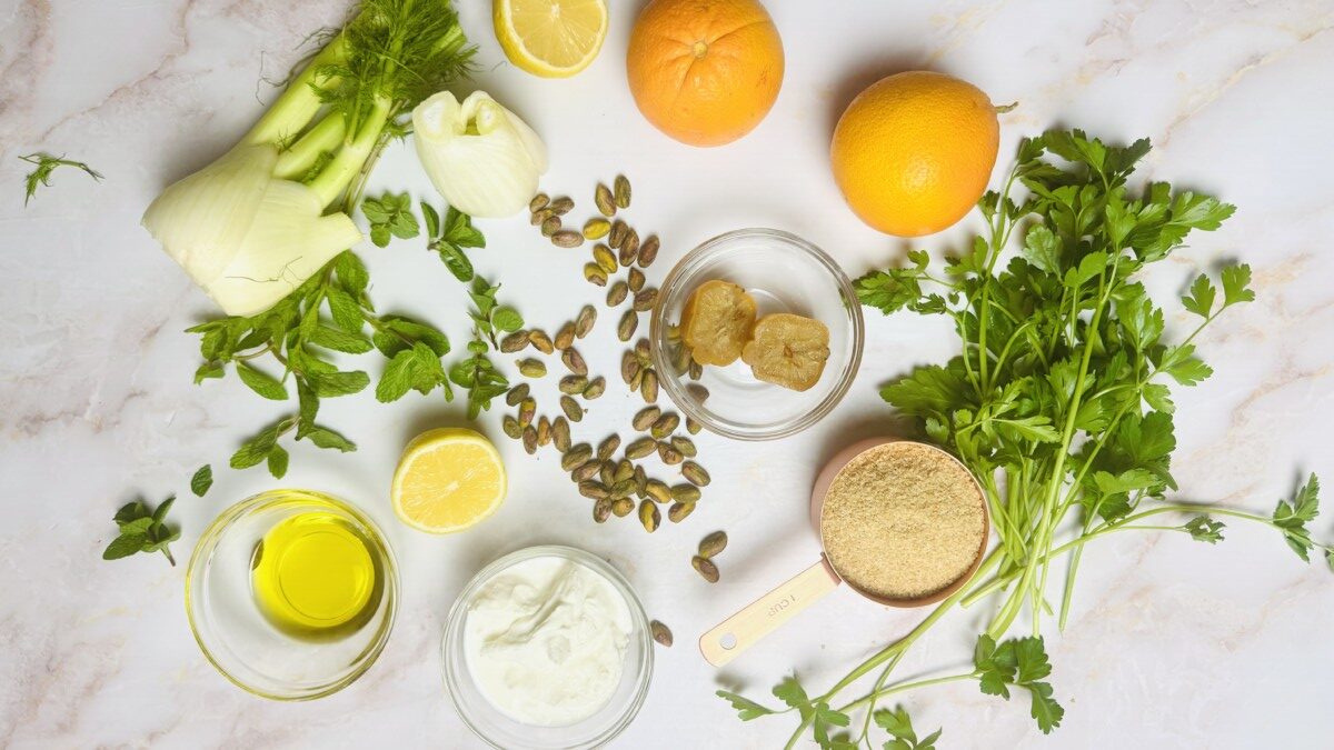 Fresh ingredients for Mediterranean Bulgur Salad, including bulgur, fennel, oranges, pistachios, herbs, and yogurt dressing, measured and ready to use.