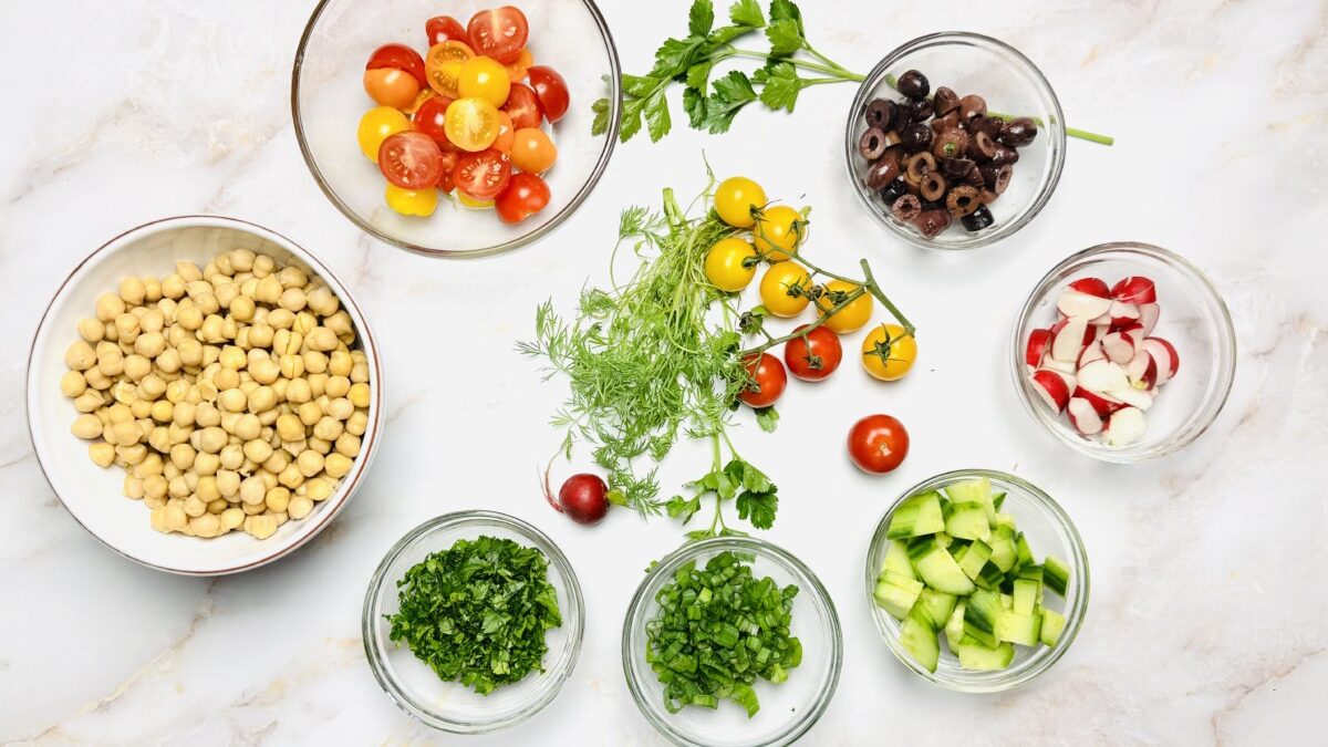 Measured ingredients for Mediterranean Garbanzo Bean Salad, including chickpeas, fresh veggies, herbs, and pomegranate molasses dressing.