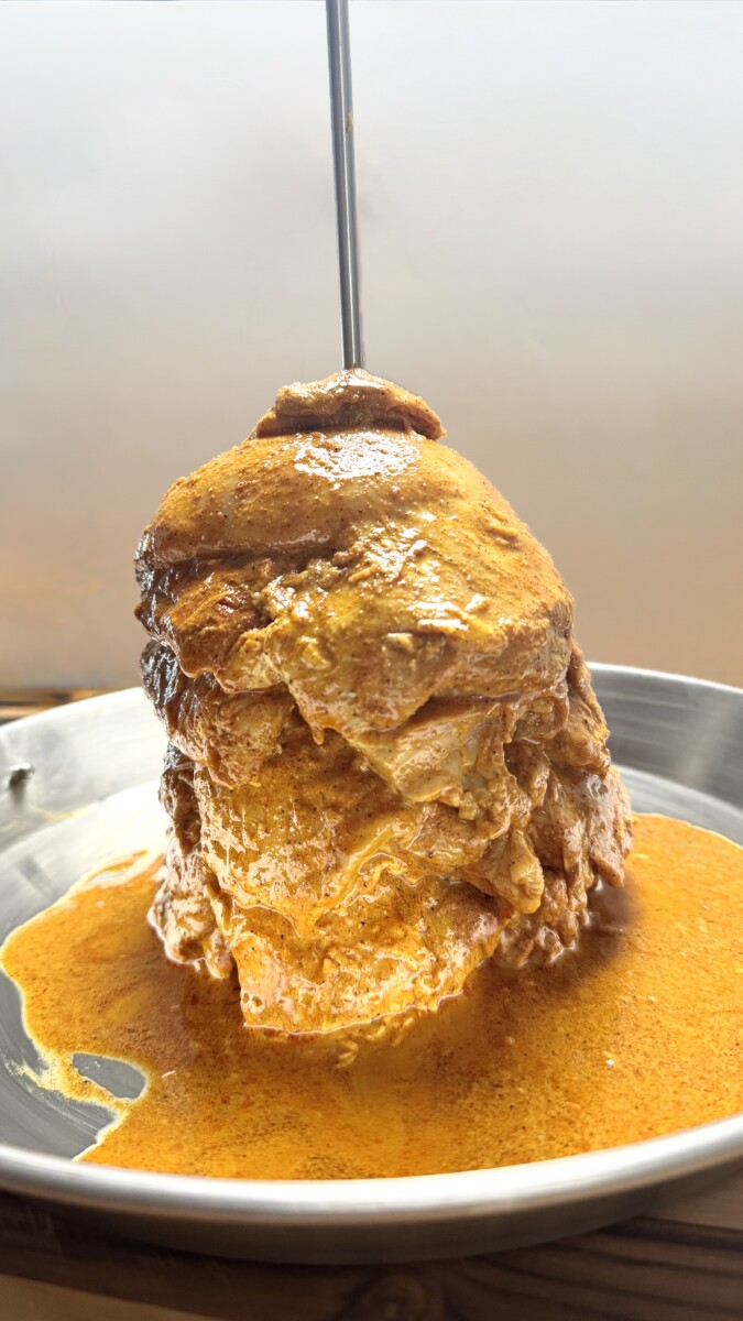 Marinated chicken thighs stacked on a vertical shawarma spit, ready to be baked in the oven for authentic chicken shawarma.
