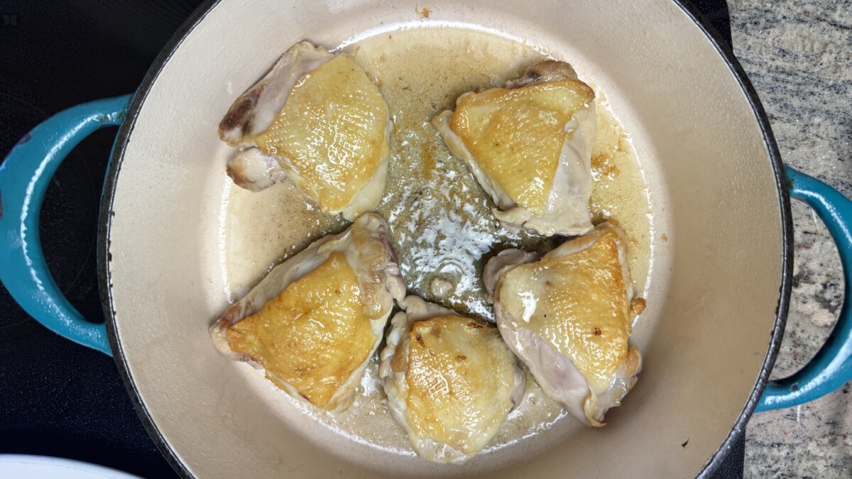 Chicken thighs sizzling in a pot, browning on one side to build flavor for Pomegranate Roasted Chicken.