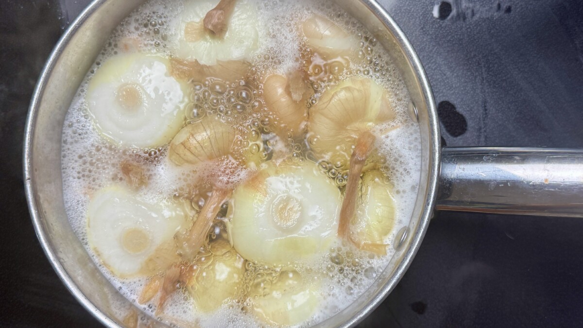 Cipollini onions simmering in a pot for a few minutes to loosen their skins, preparing for Pomegranate Roasted Chicken.