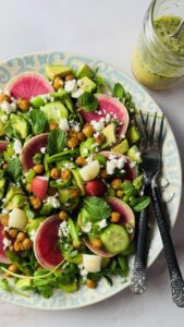 A beautifully arranged spring salad on a platter, with a jar of fresh herb dressing on the side, ready to serve.